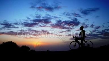 骑自行车的<strong>人站在山顶</strong>欣赏日落。 相机在Stadicam上移动。